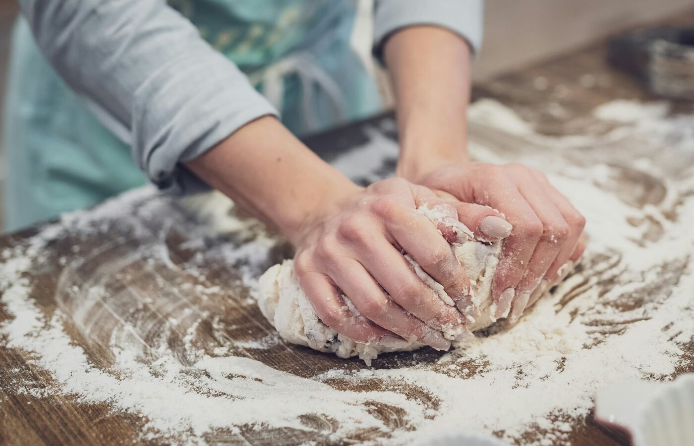Hands working dough on a flour-dusted wooden bench